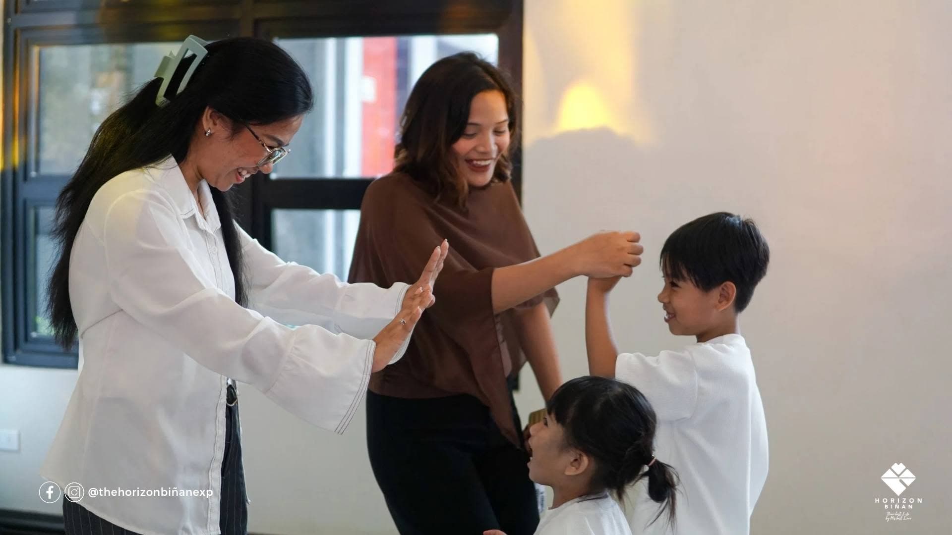 Two women sharing a joyful high five with children at Horizon Biñan.