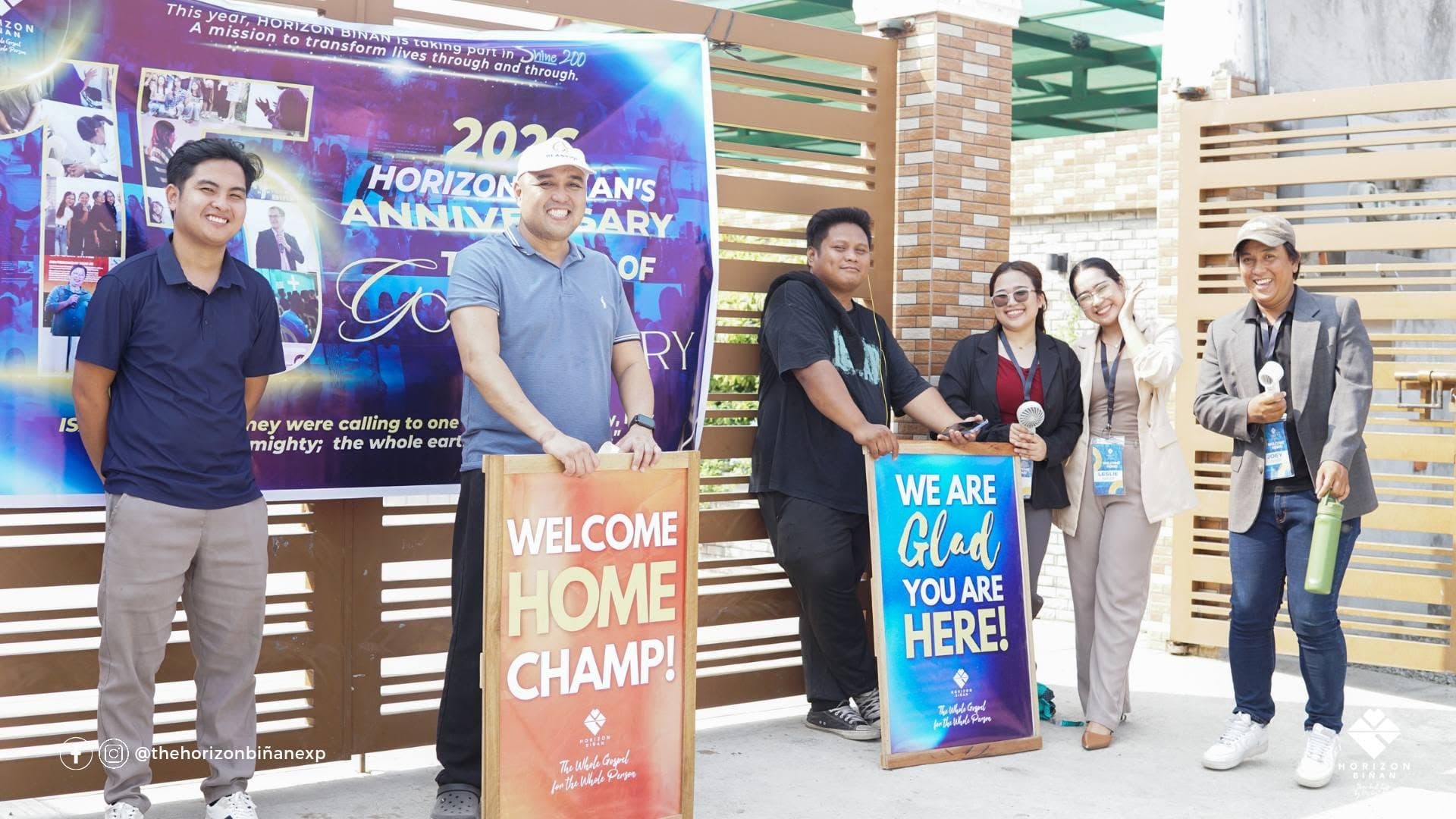 The Horizon Biñan welcome team at the church gate holding “Welcome home, champ!” and “We are glad you are here!” signs.